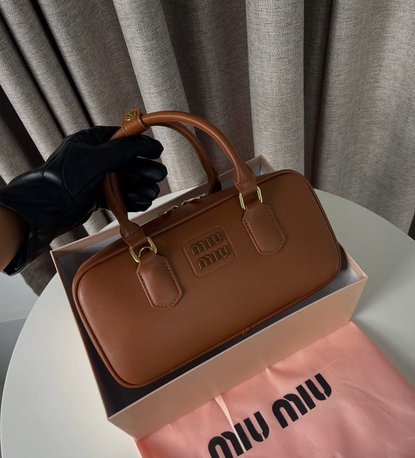 Structured cognac tan leather bauletto bag with gold hardware in a gift box.