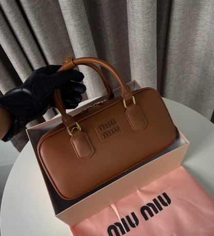 Structured cognac tan leather bauletto bag with gold hardware in a gift box.